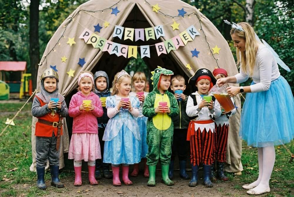Dzieci w przebraniach bajkowych piją kolorowy eliksir przemiany z kubeczków, obok nauczycielka przebrana za wróżkę