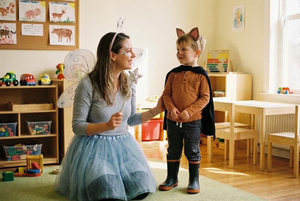 Nauczycielka przebrana za Wróżkę z foliową różdżką stoi obok dziecka w stroju Kota w Butach z dorysowanymi wąsami