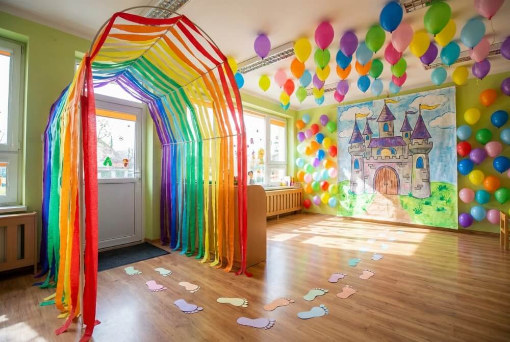 Bajkowo udekorowana sala przedszkolna z magicznym tunelem z bibuły, zamkiem na ścianie i papierowymi śladami stóp na podłodze