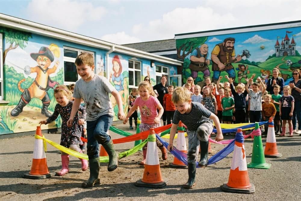 Dzieci w za dużych kaloszach pokonują tor przeszkód w sali ozdobionej motywami bajkowymi