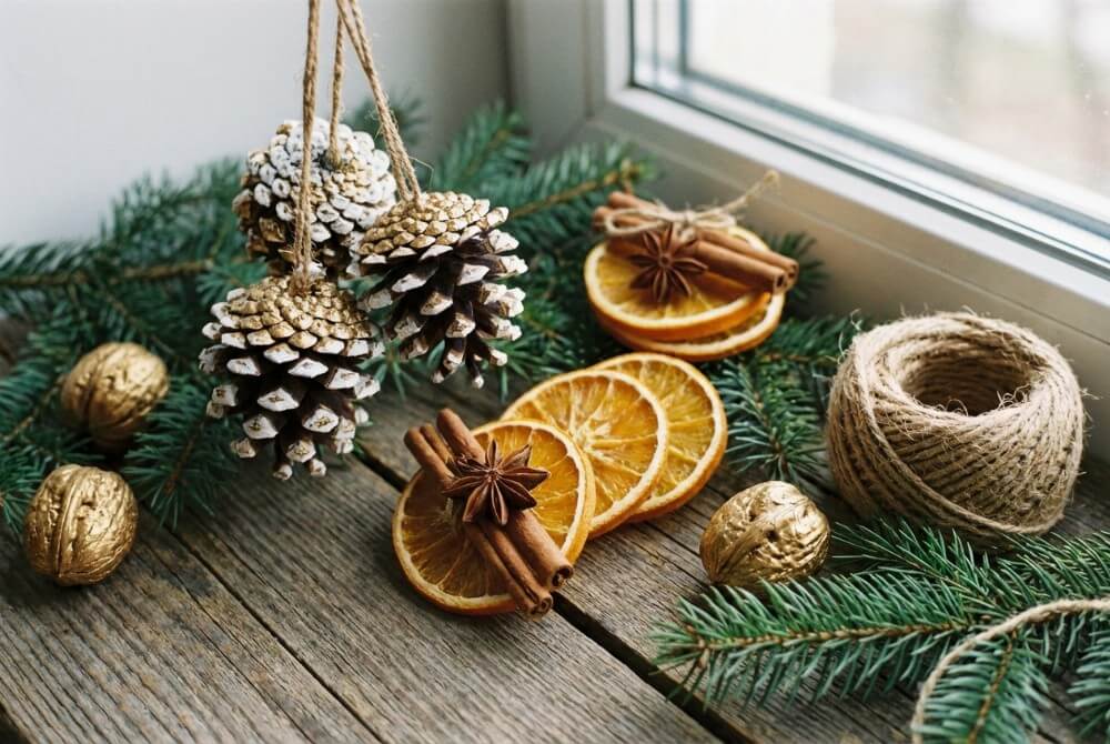 Naturalne ozdoby choinkowe z szyszek, suszonych plasterków pomarańczy z cynamonem i złoconych orzechów włoskich ułożone na drewnianym stole z gałązkami świerku.